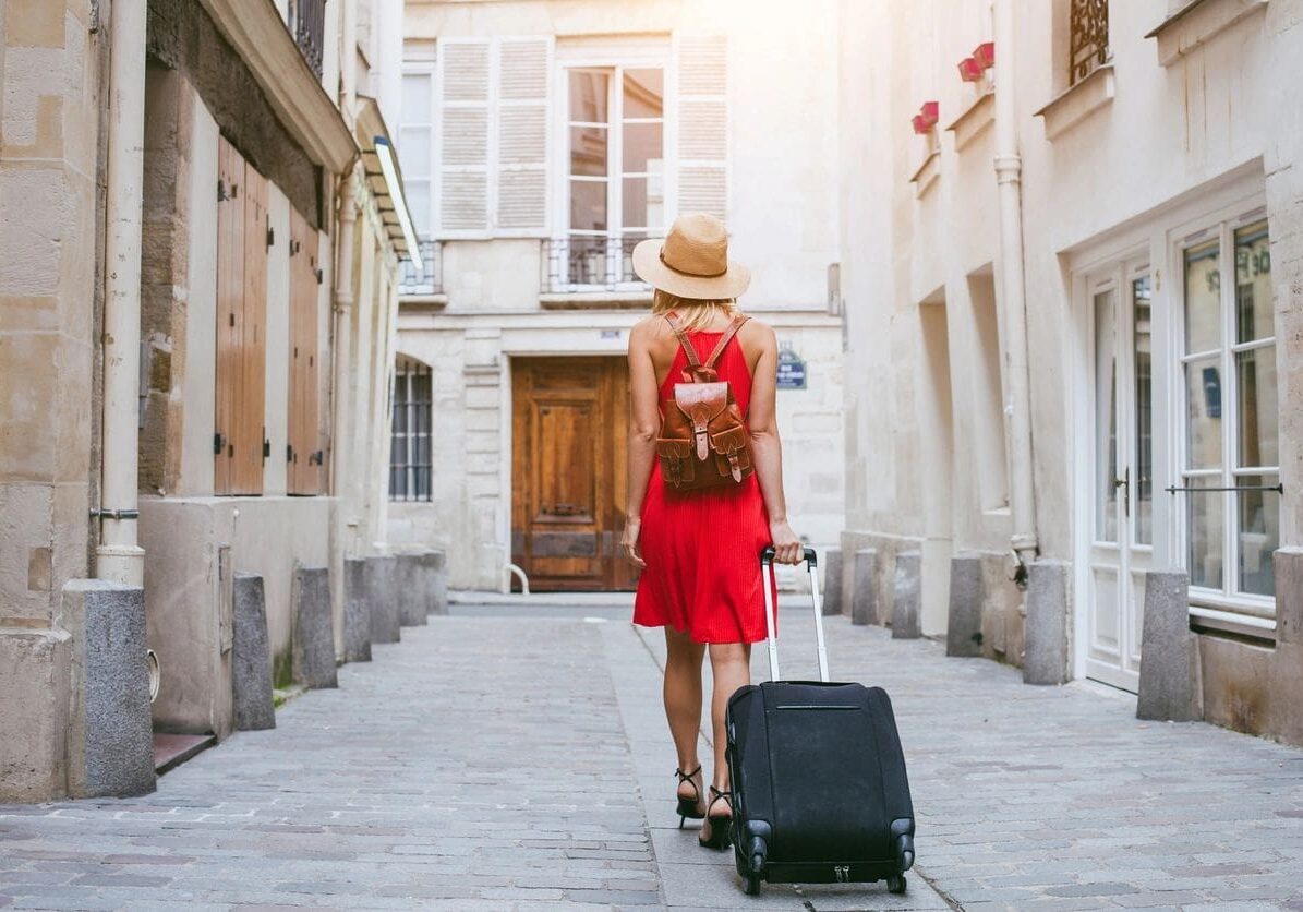 A woman in red is pulling luggage down the street.