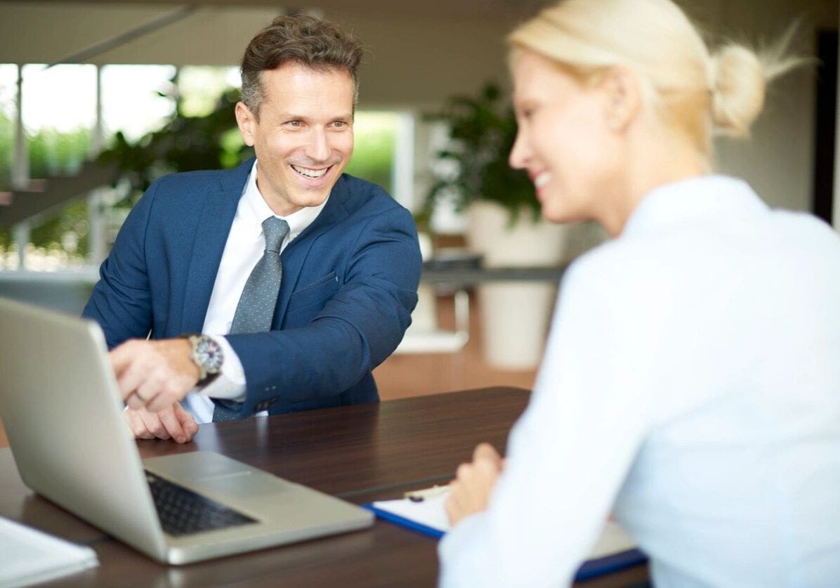 A man and woman sitting at a table with a laptop.